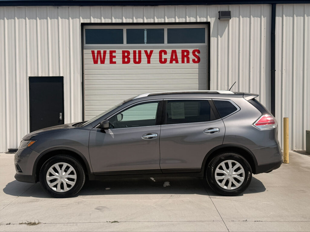 Silver SUV parked in front of a white corrugated metal building with a garage door that reads 'WE BUY CARS' in red letters.