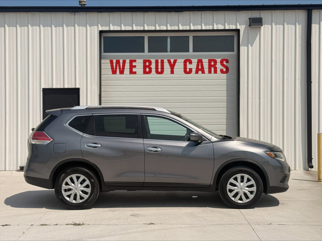 Gray SUV parked in front of a white industrial building with a garage door that reads 'WE BUY CARS' in red letters