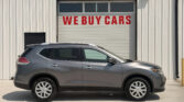 Gray SUV parked in front of a white industrial building with a garage door that reads 'WE BUY CARS' in red letters