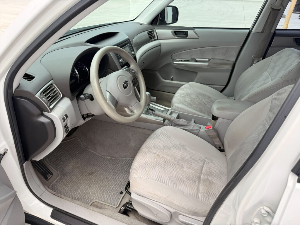 Front interior of a light-gray sedan showing steering wheel, center console, and front seats.