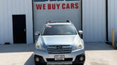 Silver SUV parked in front of a garage door with a large red 'WE BUY CARS' sign above it; car has a Wheel City license plate frame and dealership sticker visible on windshield
