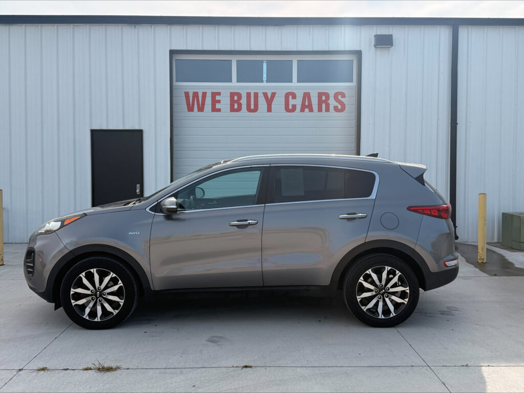Gray SUV parked in front of a light-gray industrial building with a large garage door that reads 'WE BUY CARS'